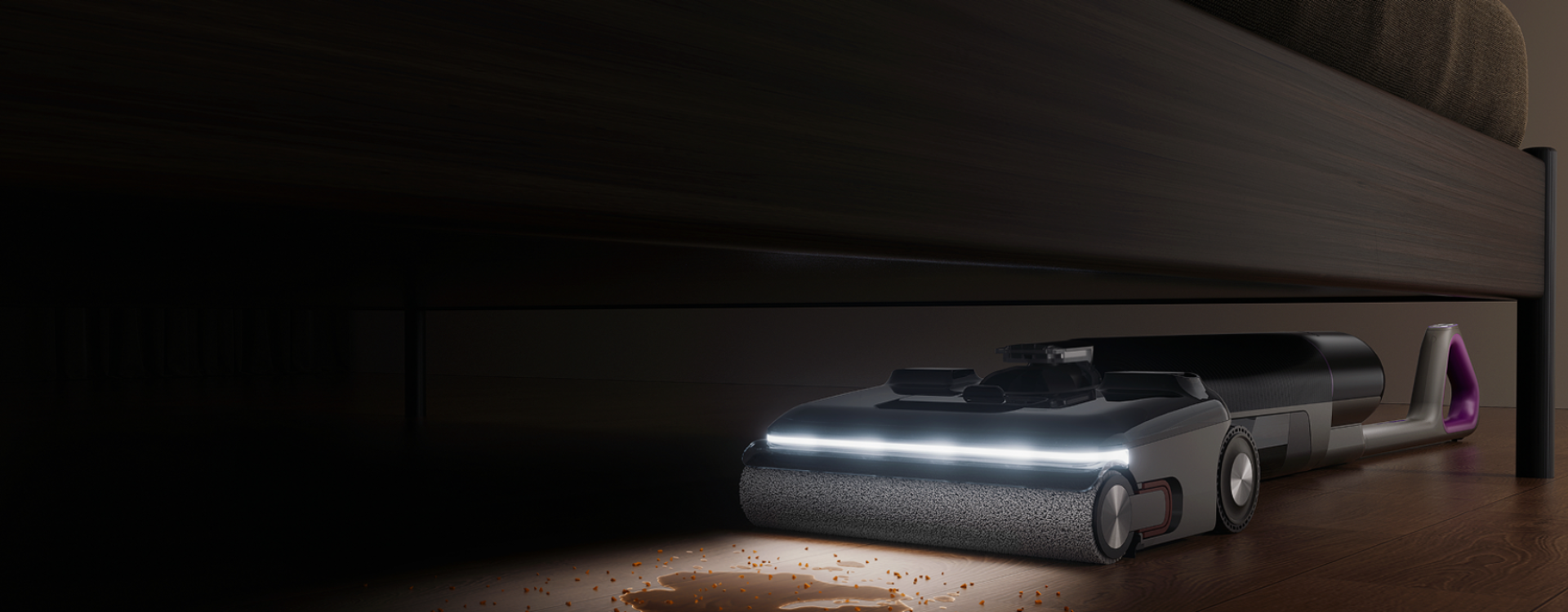 A robotic vacuum cleaner under a bed, shown in a dark bedroom environment with its front light illuminated.